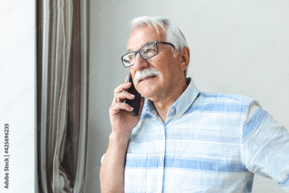 Senior man at home talking on cell phone. Cheerful man making a phone call and looking out the window Technology, communication and people concept - happy senior man calling on smartphone at home Senior man at home talking on cell phone. Cheerful man making a phone call and looking out the window Technology, communication and people concept - happy senior man calling on smartphone at home