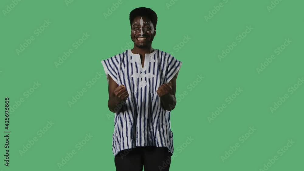 Portrait young African American man with wow surprised and delighted facial expression. Black male with an ethnic white pattern on face and in striped national shirt posing on green screen in studio. Portrait young African American man with wow surprised and delighted facial expression. Black male with an ethnic white pattern on face and in striped national shirt posing on green screen in studio.