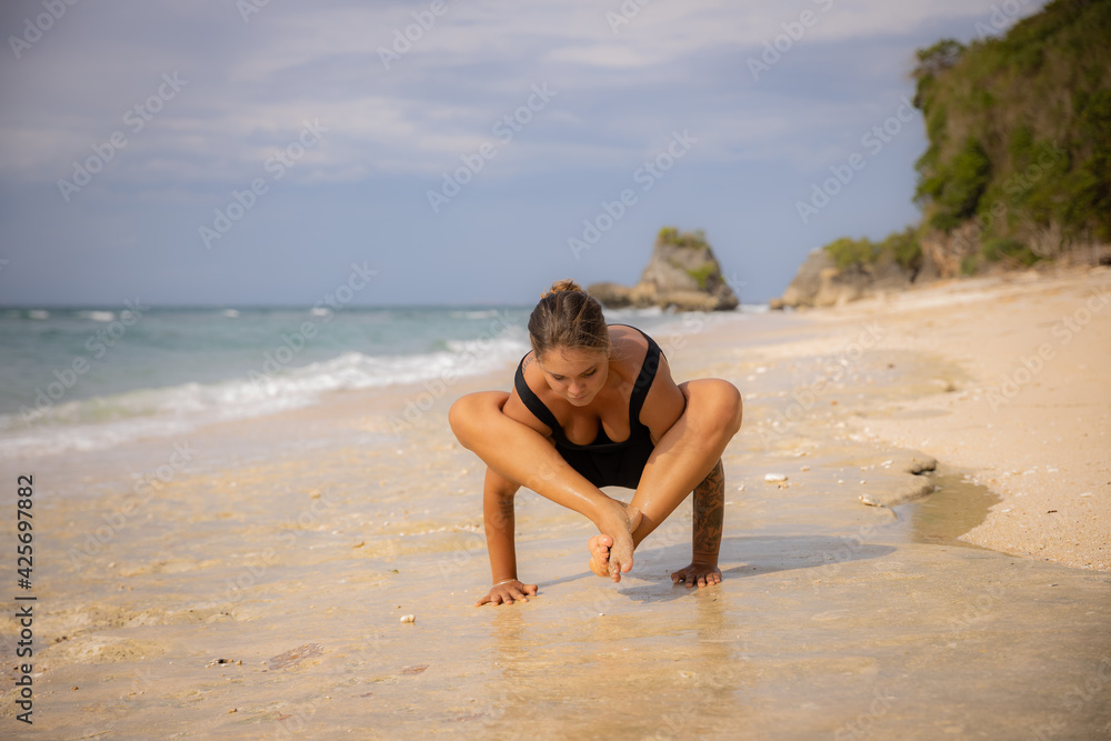 Caucasian woman practicing Bhujapidasana, Arm Pressure Balance on the beach. Strong healthy body. Self-care concept. Yoga retreat. Thomas beach, Bali