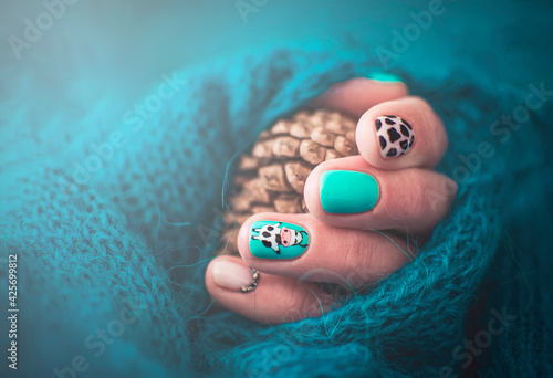 Handmade creative manicure design with farm animal motives. Cow hair texture on the nails. Summer style. Selective focus on a drawn cow, blurred background, pine cone and knitted sweater.