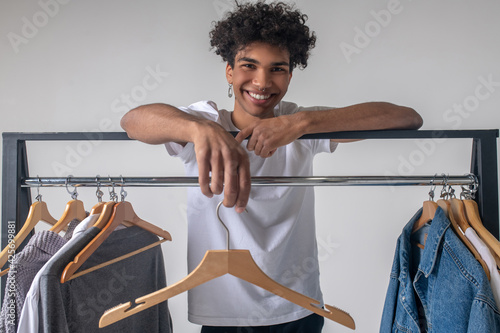 African american young guy near hangers with clothes smiling