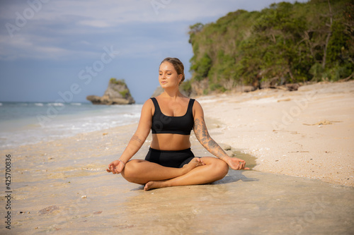 Lotus pose. Beautiful woman sitting on the sand in Padmasana. Hands in gyan mudra. Closed eyes. Yoga and meditation concept. Healthy lifestyle. Yoga retreat. Thomas beach  Bali