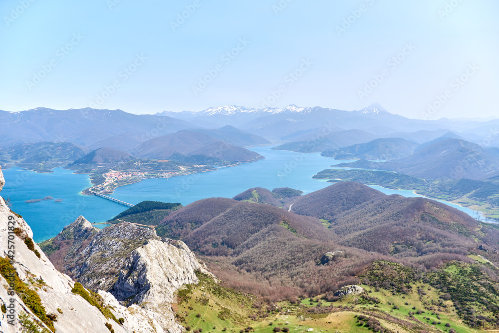 Aerial view from the Gilbo peak towards the Riaño reservoir, the village and the Picos de Europa. Snow on top of the mountains. Spring in León