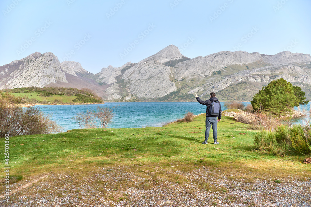 Man on the right of a meadow, turquoise blue water of the marsh and mountains in the background. Man on the right of a meadow, turquoise blue water of the marsh and mountains in the background.