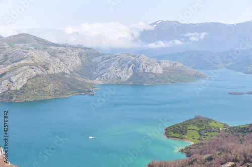 Aerial view of the Ria  o reservoir with a boat sailing its turquoise blue waters surrounded by mountains in spring.