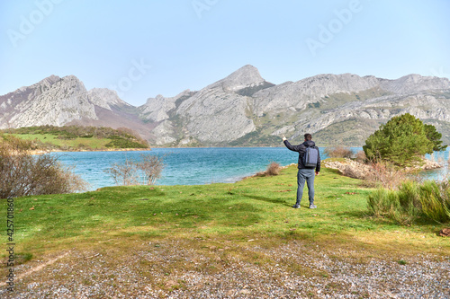 Man on the right of a meadow, turquoise blue water of the marsh and mountains in the background. 