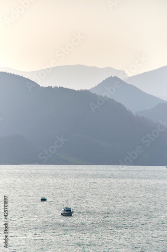 Vertical wallpaper of a ship at sea with mountains in the background at sunrise. Silhouette of a boat and mountains with pastel colours.