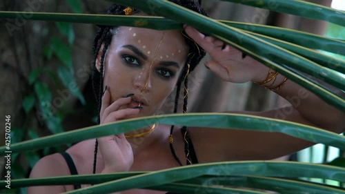 A girl with beautiful bright trible makeup smoothly moves dance her hands, framed by palm trees