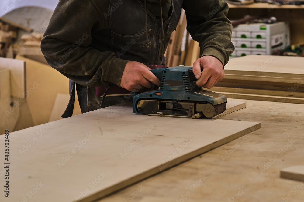 Close up. Carpenter at workshop polishes wooden board with a electric orbital sander. Woodwork and furniture making concept. Close up. Carpenter at workshop polishes wooden board with a electric orbital sander. Woodwork and furniture making concept.