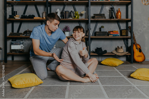 Couple doing Yoga at home in pajamas near bookshelf. Young man and woman doing sports at home.