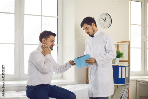 Young man wearing cervical collar seeing doctor at clinic or hospital. Professional traumatologist with clipboard helping male patient with broken neck. Examination and injury treatment after accident