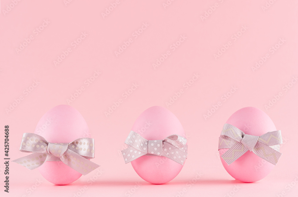 Pink easter eggs with grey bows standing in row on pastel pink background.