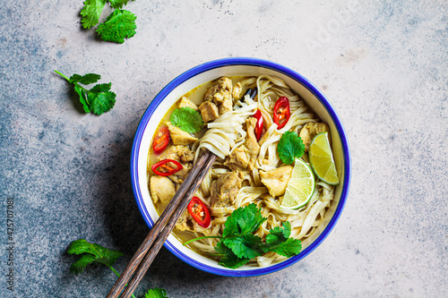 Thai green curry noodles with chicken, chili and cilantro in white bowl.
