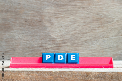 Tile letter on red rack in word PDE (abbreviation of permitted daily exposure, partial differential equation or personal development education) on wood background