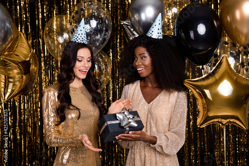 Photo of two glamour brunette girls give gift wear cone hat balloons party isolated on shine bright tinsel background