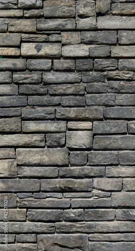 big dark wall with black and gray irregular bricks of stone - vertical background texture 