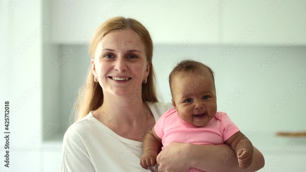 Woman posing and holding small baby in arms, standing in home room spbd. Woman posing and holding small baby in arms, standing in home room spbd.
