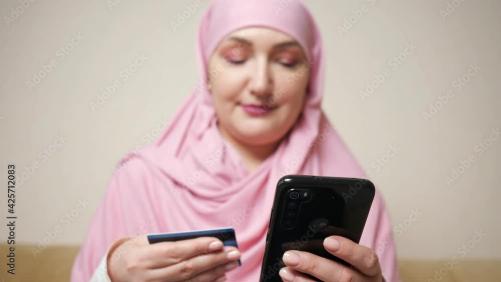 Woman in a pink scarf makes online purchases on the phone with a bank card in hands. Woman in a pink scarf makes online purchases on the phone with a bank card in hands.