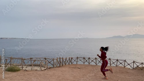 Great physical activity. Active young woman enjoying the view while jogging along the cliff edge at sunrise. Slow motion. Copy space. Body positive, healthy lifestyle, nature concept
