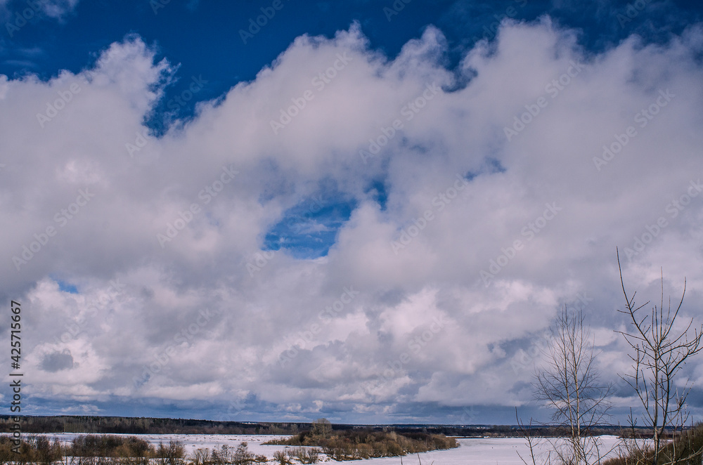 Obraz premium Winter landscape with a high bank of the river covered with ice, cumulus clouds in the sky,.deep snow cover with footprints, a clear horizon line, toned.