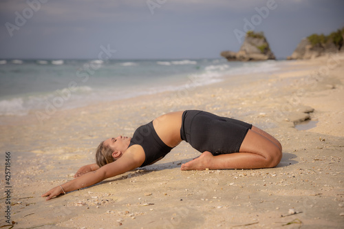 Yoga practice on the beach. Caucasian woman practicing Paripurna Ustrasana, Full Camel Pose. Kneeling back bending asana. Flexible spine. Yoga retreat. Healthy lifestyle. Thomas beach, Bali