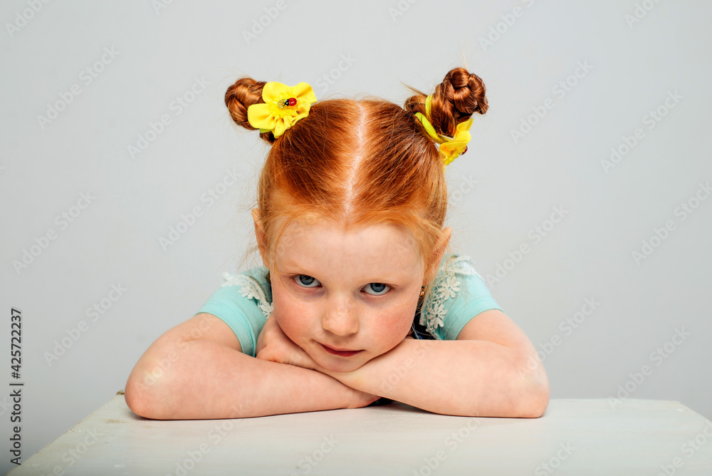 Little girl with red hair on a gray background. Sad. She put her head ...