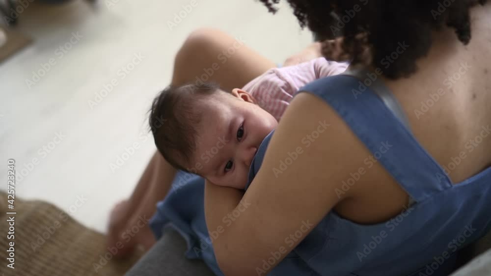 Young mother breastfeeding daughter and sitting on couch in apartment room spbd.