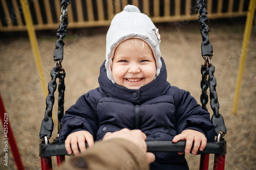 Smiling portrait of a child on a swamp on the territory of a children's playground with an adult in warm clothes in the fall. Emotions from walking in the fresh air.