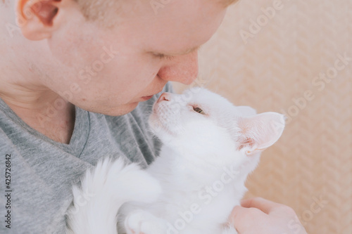 Young Caucasian blond male holding a white cat in his arms. The concept of love for pets, a cat's trust in humans..