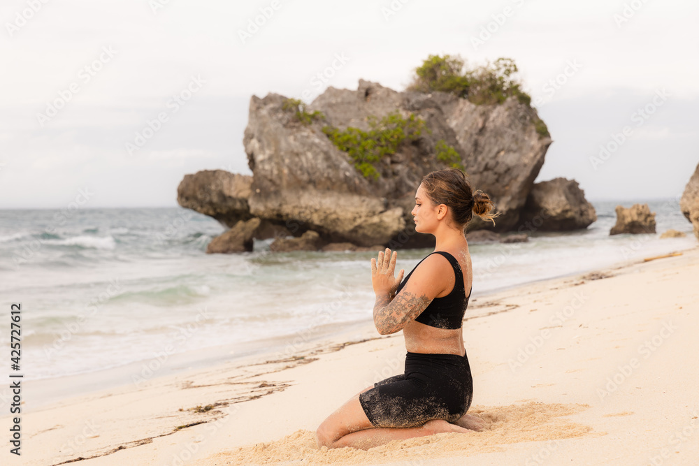Diamond Pose, Vajrasana sitting yoga pose. Caucasian woman practicing yoga on the beach. Hands in namaste mudra. Fit body. Self-care concept. Yoga retreat. Thomas beach, Bali