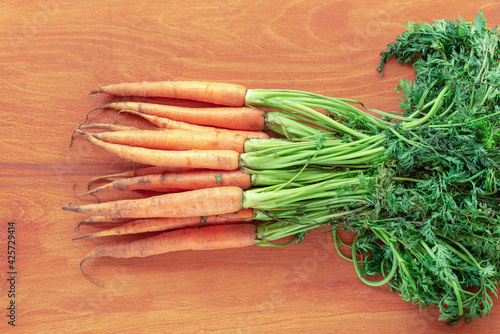 Fresh organic carrot with green leaves on orange wooden table, top view, flat lay