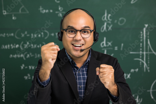 Indian young teacher man looking at camera sitting teaching online video conference live stream. Asian teacher wearing headset teaching class webinar online for students learning.