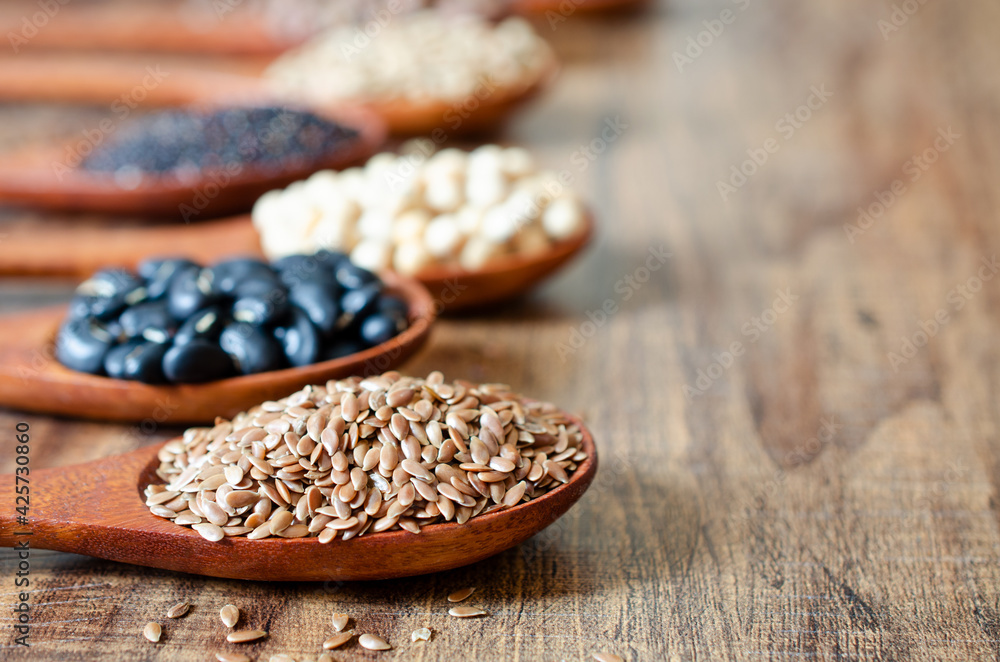 Obraz premium Closed up dry organic flax seed in wooden spoon with blur black bean, soybean, quinoa, and chickpea, for healthy food or agricultural product concept