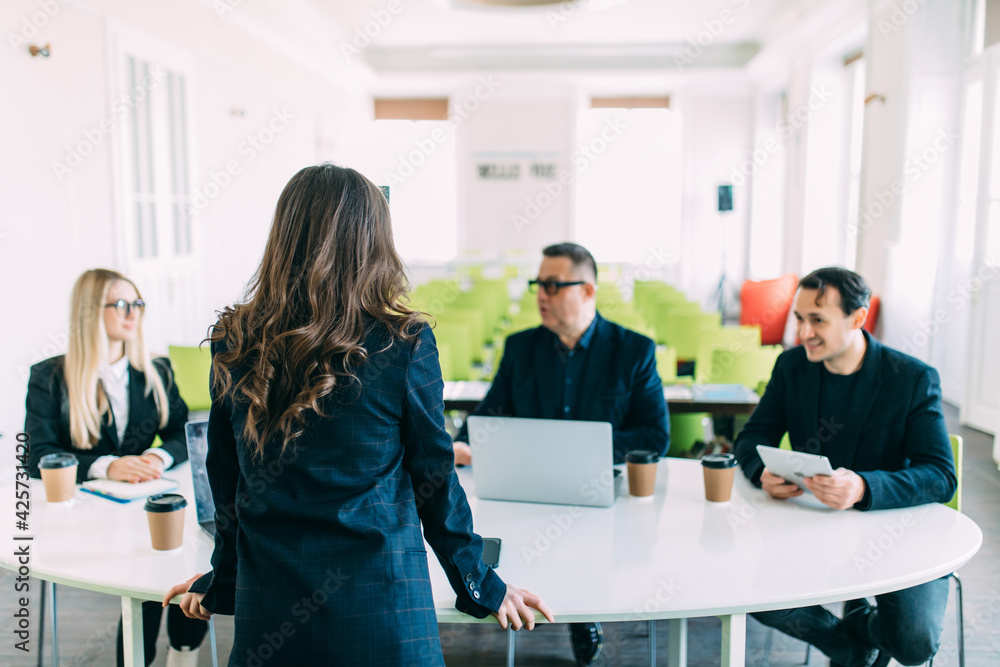 Confident businesswoman commenting marketing results to colleagues at meeting. Rear view. Confident businesswoman commenting marketing results to colleagues at meeting. Rear view.