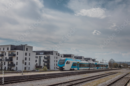 Modern white and blue passenger train on a station in front of a modern housing or residental district. City blocks and train.