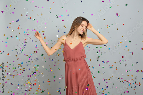 Happy woman and falling confetti on light grey background