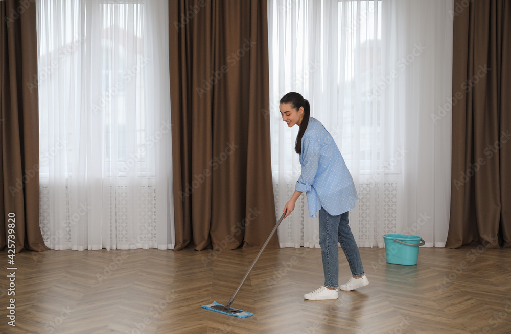 Fototapeta premium Young woman cleaning floor with mop in empty room