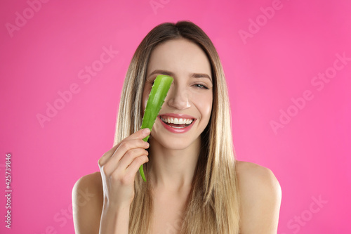 Happy young woman with aloe leaf on pink background
