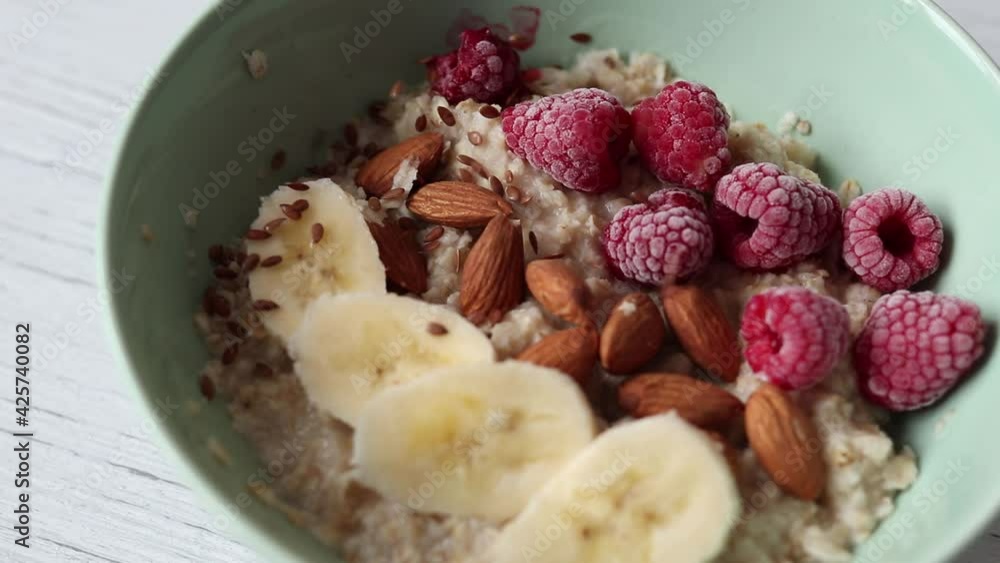 Decorating oatmeal with fruit and nuts flax seeds, close-up slow motion video Decorating oatmeal with fruit and nuts flax seeds, close-up slow motion video