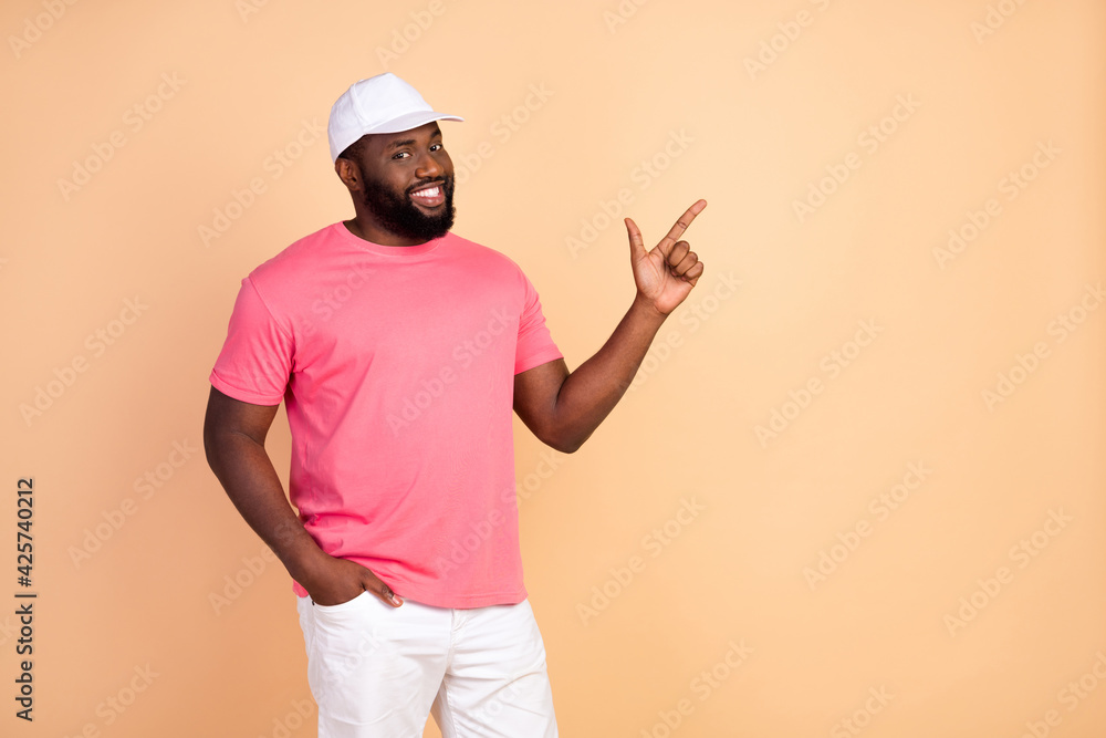 Photo portrait of man wearing casual clothes cap smiling pointing finger empty space isolated pastel beige color background