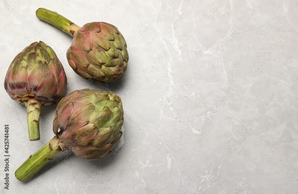 Fototapeta premium Fresh raw artichokes on grey marble table, flat lay. Space for text