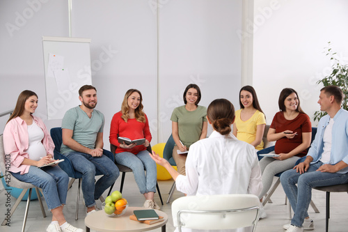 Group of pregnant women with men and doctor at courses for expectant parents indoors