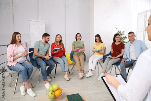 Group of pregnant women with men and doctor at courses for expectant parents indoors