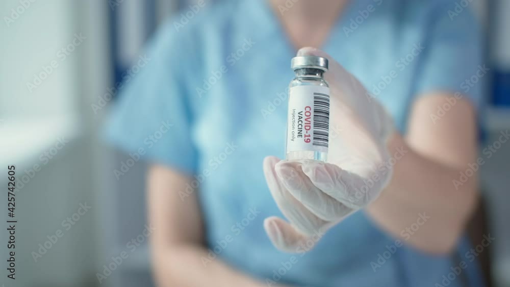 covid-19 vaccination, medical worker in a blue uniform and protective gloves holds a vaccine in glass bottle at the hospital, selective focus covid-19 vaccination, medical worker in a blue uniform and protective gloves holds a vaccine in glass bottle at the hospital, selective focus