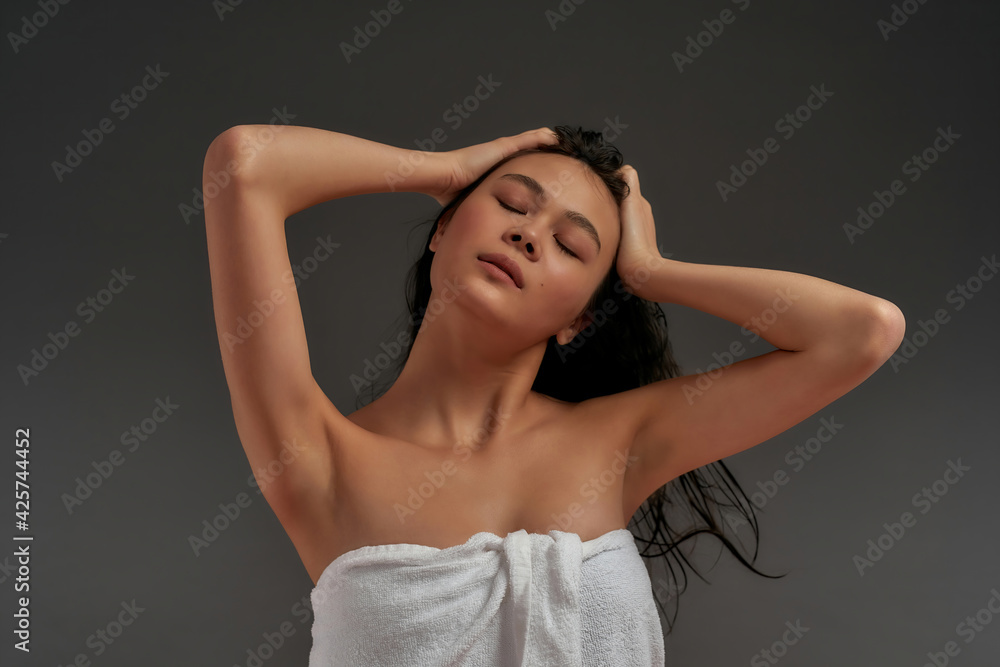 Young beautiful asian half naked woman tousled her hair in bath towel with eyes closed