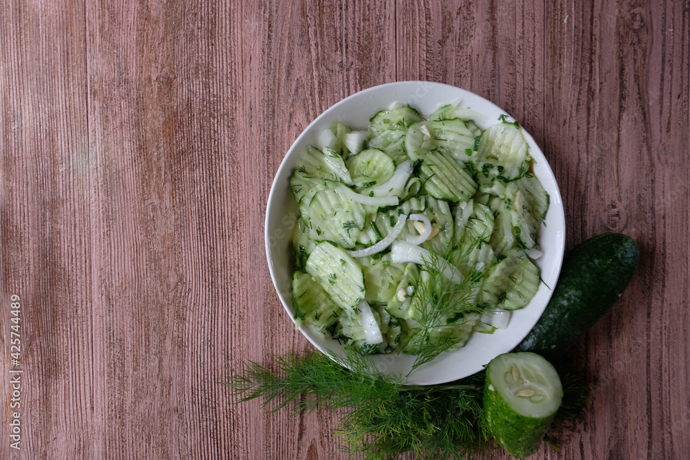 A delicious salad of fermented cucumbers with onions and dill in a white plate on a wooden background. Concept -home-made for the winter. Copy space. Healthy diet. A delicious salad of fermented cucumbers with onions and dill in a white plate on a wooden background. Concept -home-made for the winter. Copy space. Healthy diet.