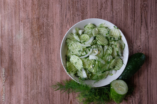 A delicious salad of fermented cucumbers with onions and dill in a white plate on a wooden background. Concept -home-made for the winter. Copy space. Healthy diet.