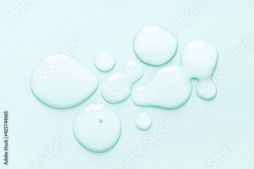 Hyaluronic acid serum drops on turquoise background.