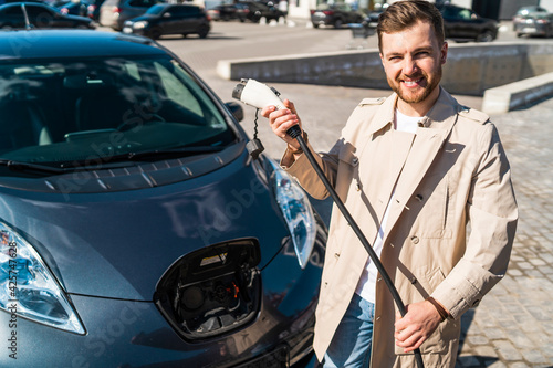 Portrait of stylish man with electric car charging connector in hands