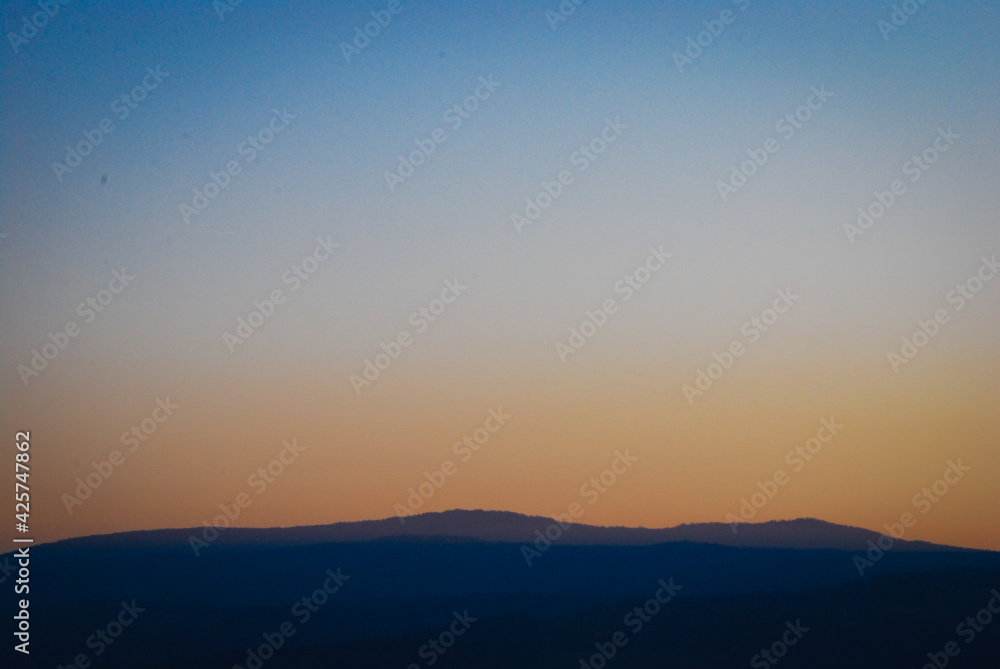 Mountain silhouette in dusk showing blue to orange sky gradient background Mountain silhouette in dusk showing blue to orange sky gradient background